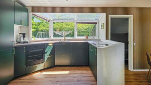 A modern kitchen with dark cabinets, a built-in oven, and a window overlooking a garden. - Stunning home in Oksbøl with sauna (Oksbøl)
