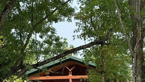 A wooden cabin with a porch, surrounded by trees and a stone wall. - Cozy Riverfront Fish Cabin (Paris)