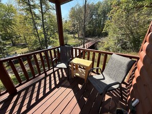 A wooden deck with a table and chairs, surrounded by a railing, overlooking a forested area.