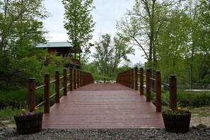 A wooden bridge leading to a building with a green roof, surrounded by trees and greenery.