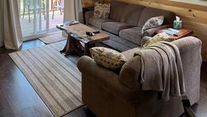 A cozy living room with a ceiling fan, wooden walls, a sofa, a coffee table, and mounted animal heads. - Cozy Riverfront Fish Cabin (Paris)