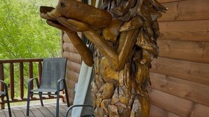 A wooden sculpture on a porch with chairs and a view of greenery. - Cozy Riverfront Fish Cabin (Paris)
