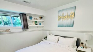 Ein modernes Schlafzimmer mit einem großen Bett, einem Nachttisch, einem an der Wand befestigten Regal mit Dekoration und einem Fenster mit Vorhängen.