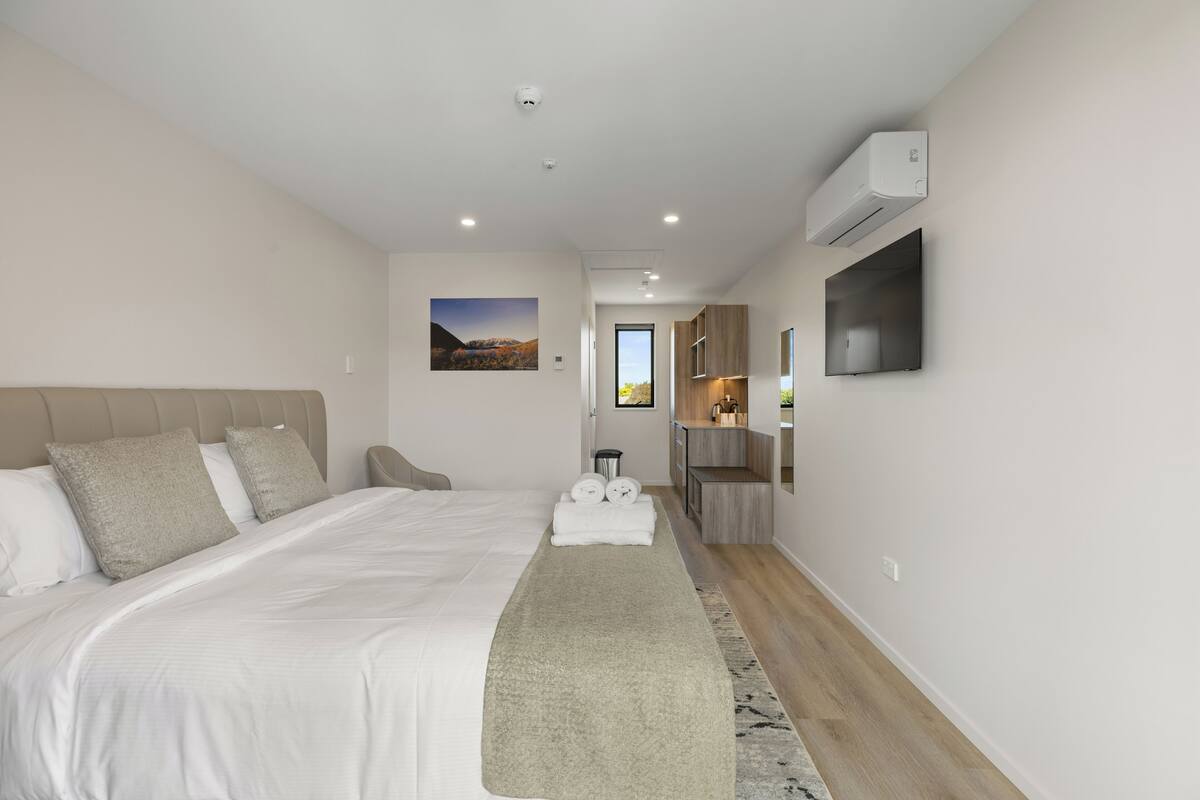 Una habitación de hotel moderna con una cama grande, una kitchenette pequeña y un baño visible a través de una puerta abierta.