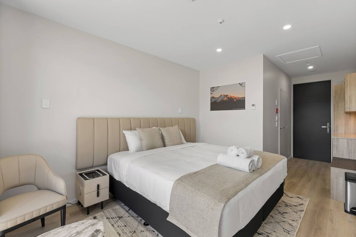 Un dormitorio moderno con una cama grande, mesitas de noche, una silla y un armario.