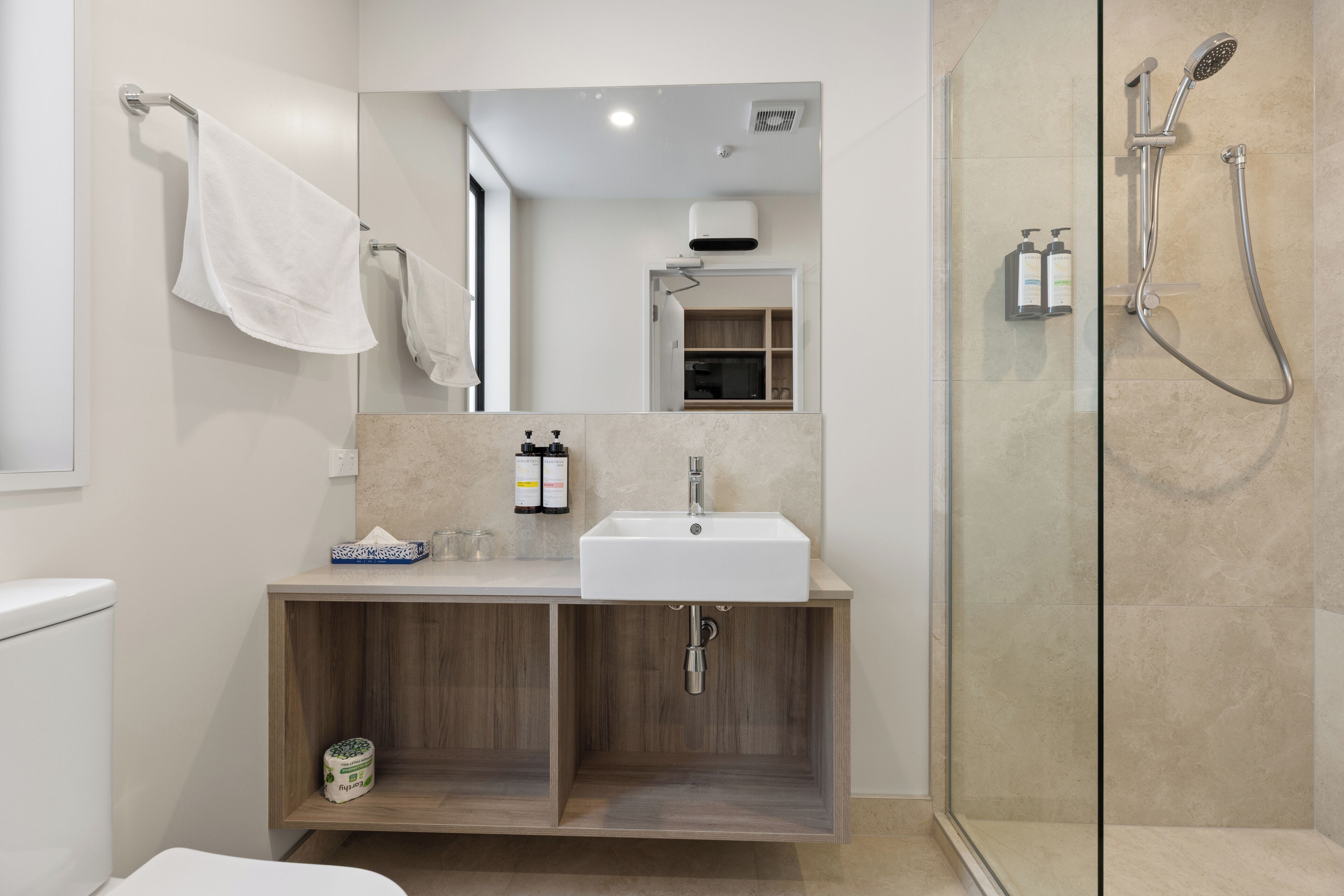 Een moderne badkamer met een douche in glazen cabine, een houten wastafelmeubel met een wastafel en een spiegel erboven.