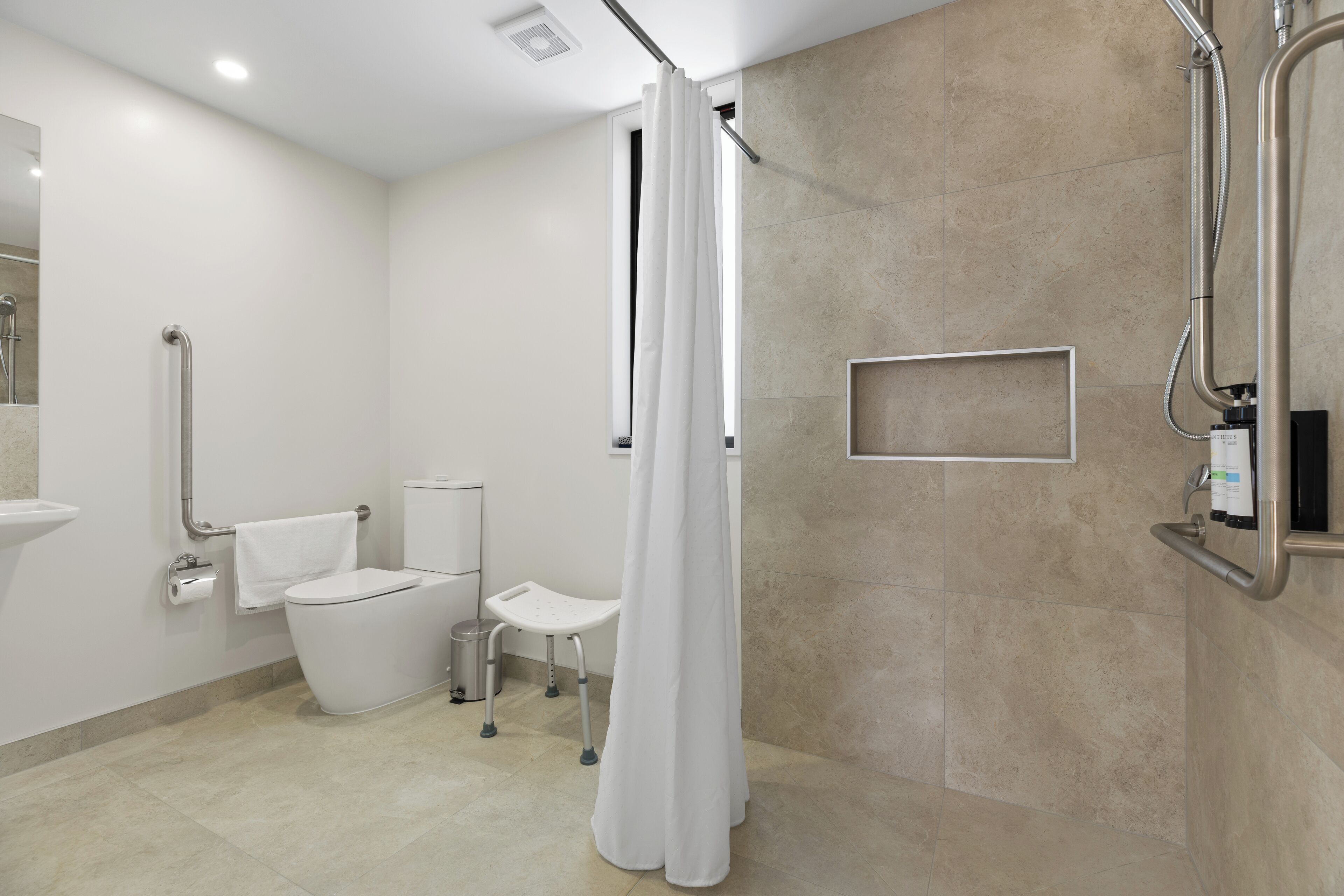 A modern bathroom with a toilet, bidet, and shower area, including grab bars and a white shower curtain.