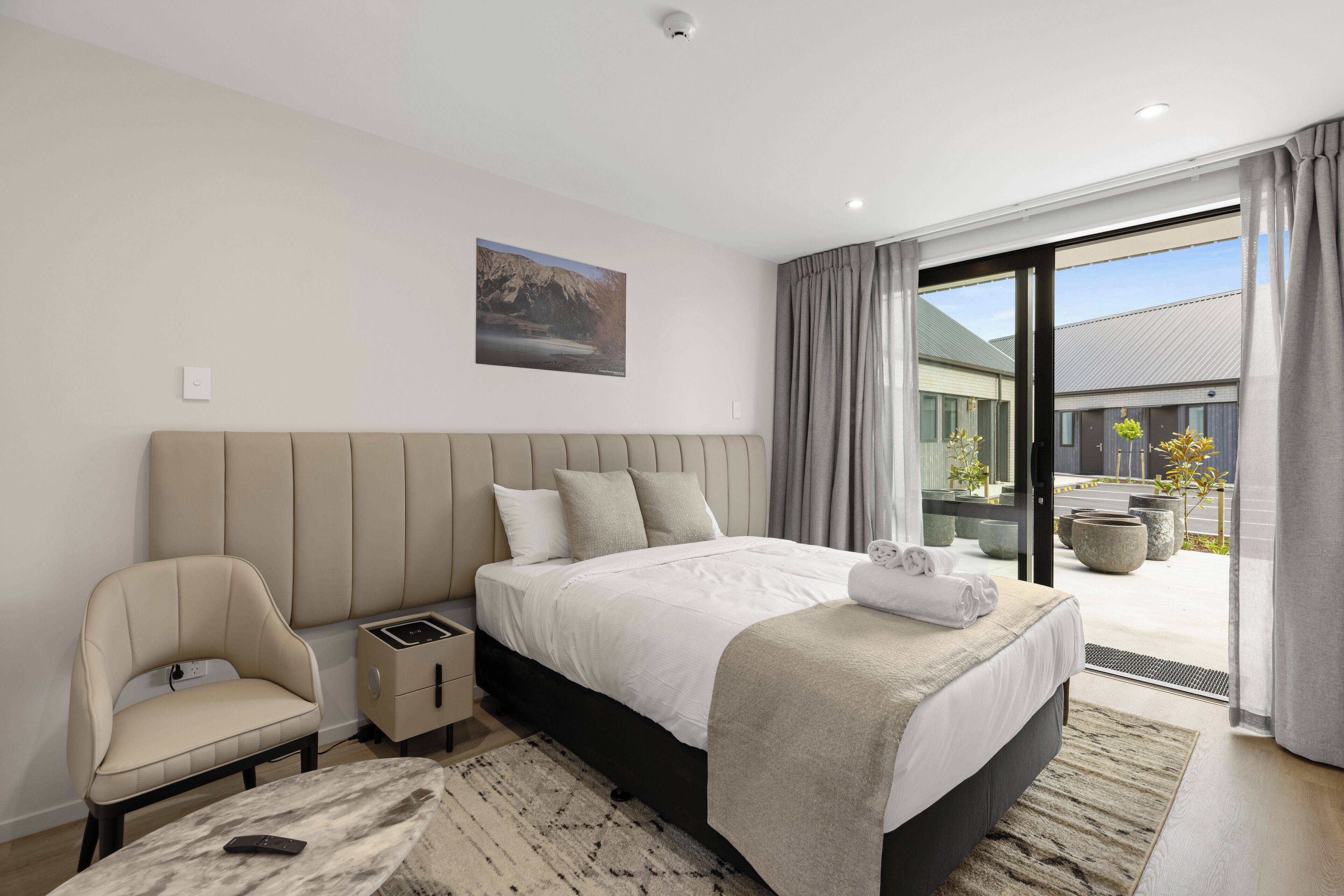 Une chambre à coucher moderne avec un grand lit, une table de chevet, une chaise et une vue sur l’extérieur.
