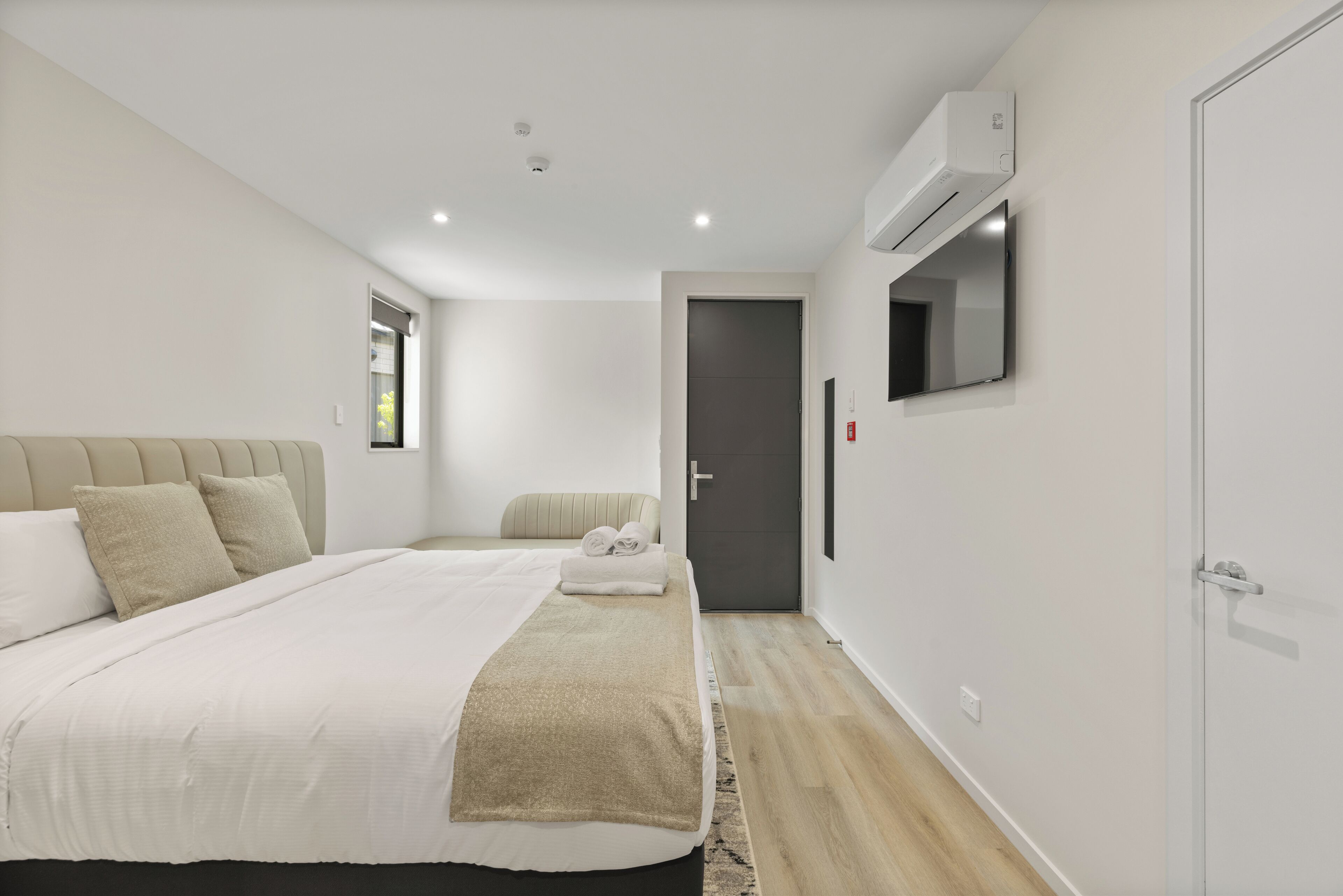 Un dormitorio moderno con una cama grande, una mesita de noche, aire acondicionado instalado en la pared y una puerta que da a otra habitación.
