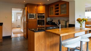 Een moderne keuken met houten kasten, roestvrijstalen apparatuur en een centraal kookeiland met barkrukken.