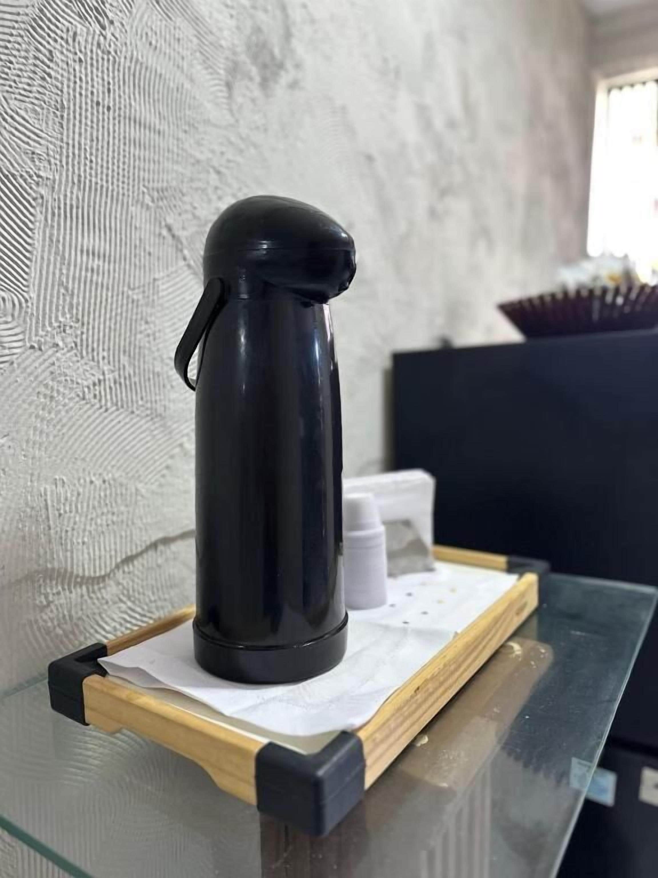 A black thermos on a glass table with a wooden tray, white bottles, and a black box in the background.