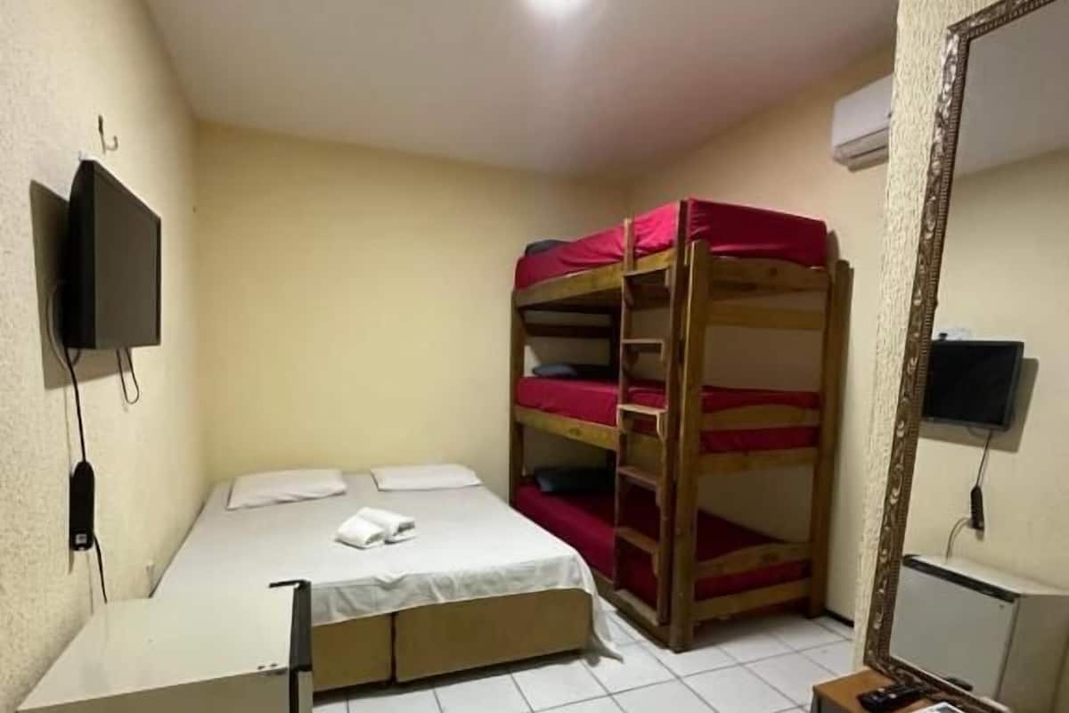 Una habitación pequeña con literas, un escritorio, un espejo y un televisor montado en la pared.