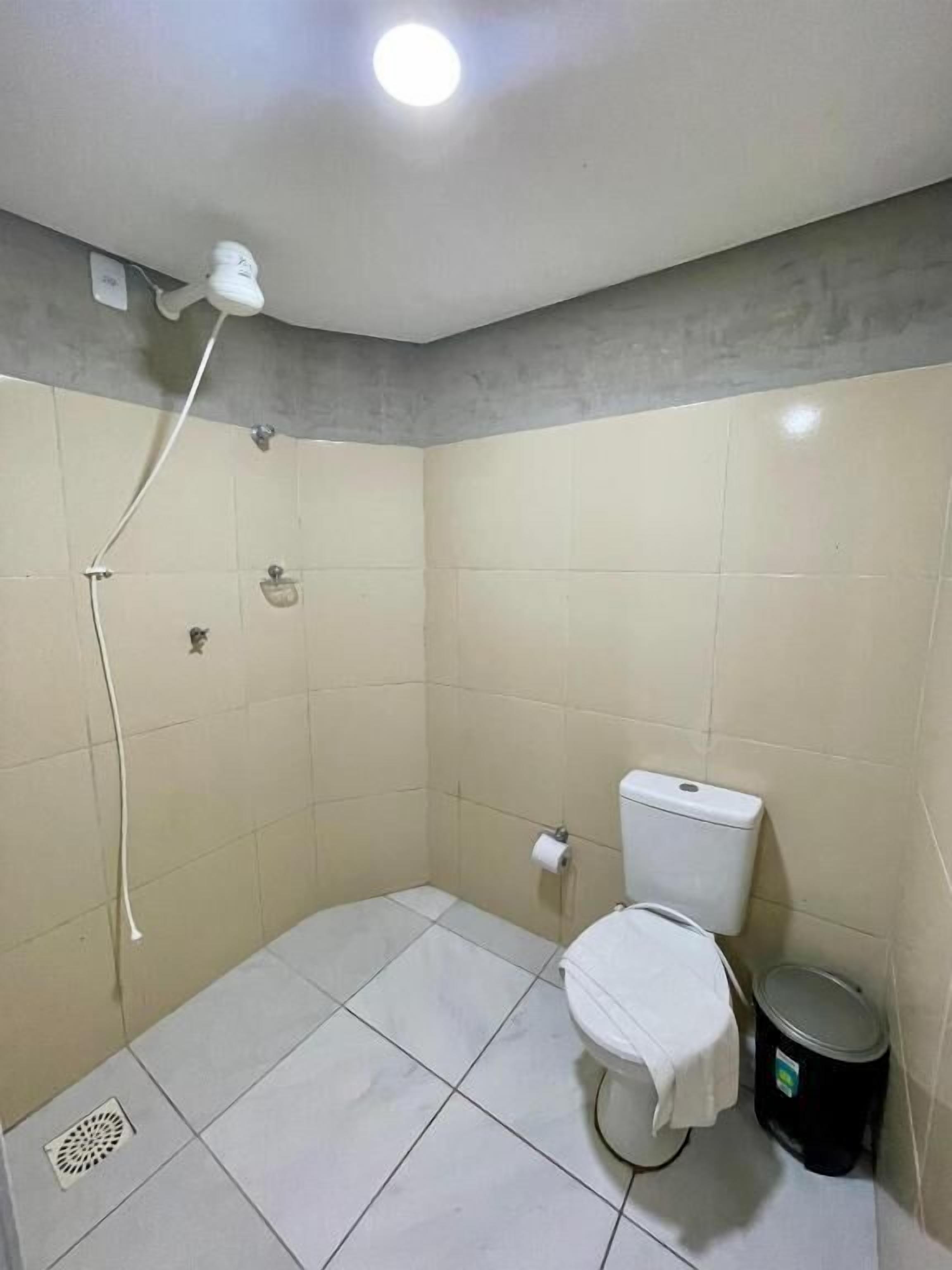 A small, tiled bathroom with a shower, toilet, and a trash bin.