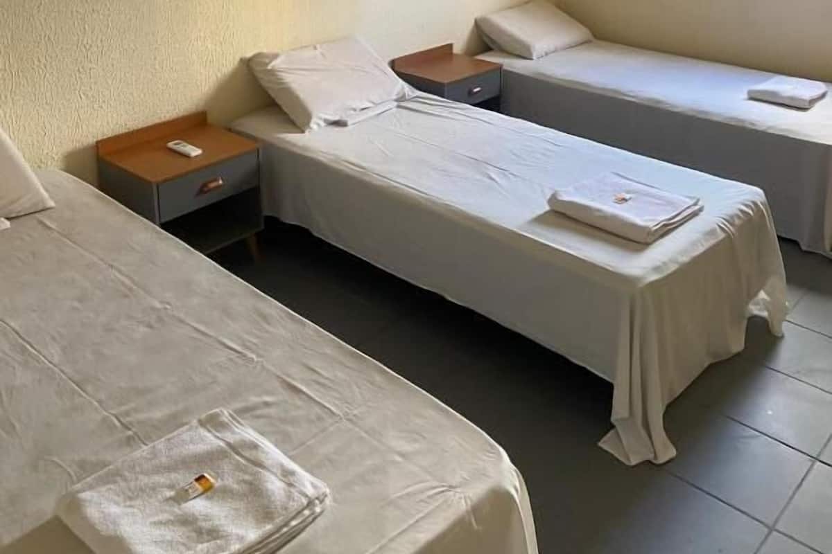 Habitación de hotel con dos camas individuales, una mesita de noche con lámpara, ventana con vistas y aire acondicionado.