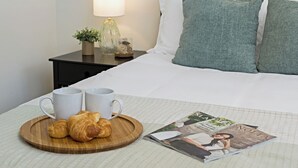 Una cama bien tendida con una revista, dos tazas y croissants en una bandeja.