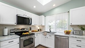 Una cocina moderna con armarios blancos, electrodomésticos de acero inoxidable y una ventana con vistas a zonas verdes.