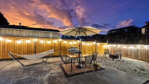 Un patio exterior con una hamaca, mesa de comedor, sillas y una parrilla.