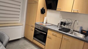 A compact kitchen with wooden cabinets, a built-in oven, a sink, and a window with blinds. - Modern & cozy apartment opposite the Deister (Barsinghausen)