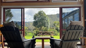 Una habitación con dos sillas negras y una mesa de madera, ventanas amplias con vistas a un paisaje verde y colinas.
