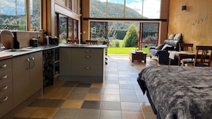 Una cocina moderna con una isla grande, un comedor con mesa y sillas, un sofá y vistas a un jardín exuberante y montañas.