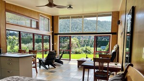 Una habitación amplia con ventanas grandes, un ventilador de techo y vistas a un jardín exuberante.