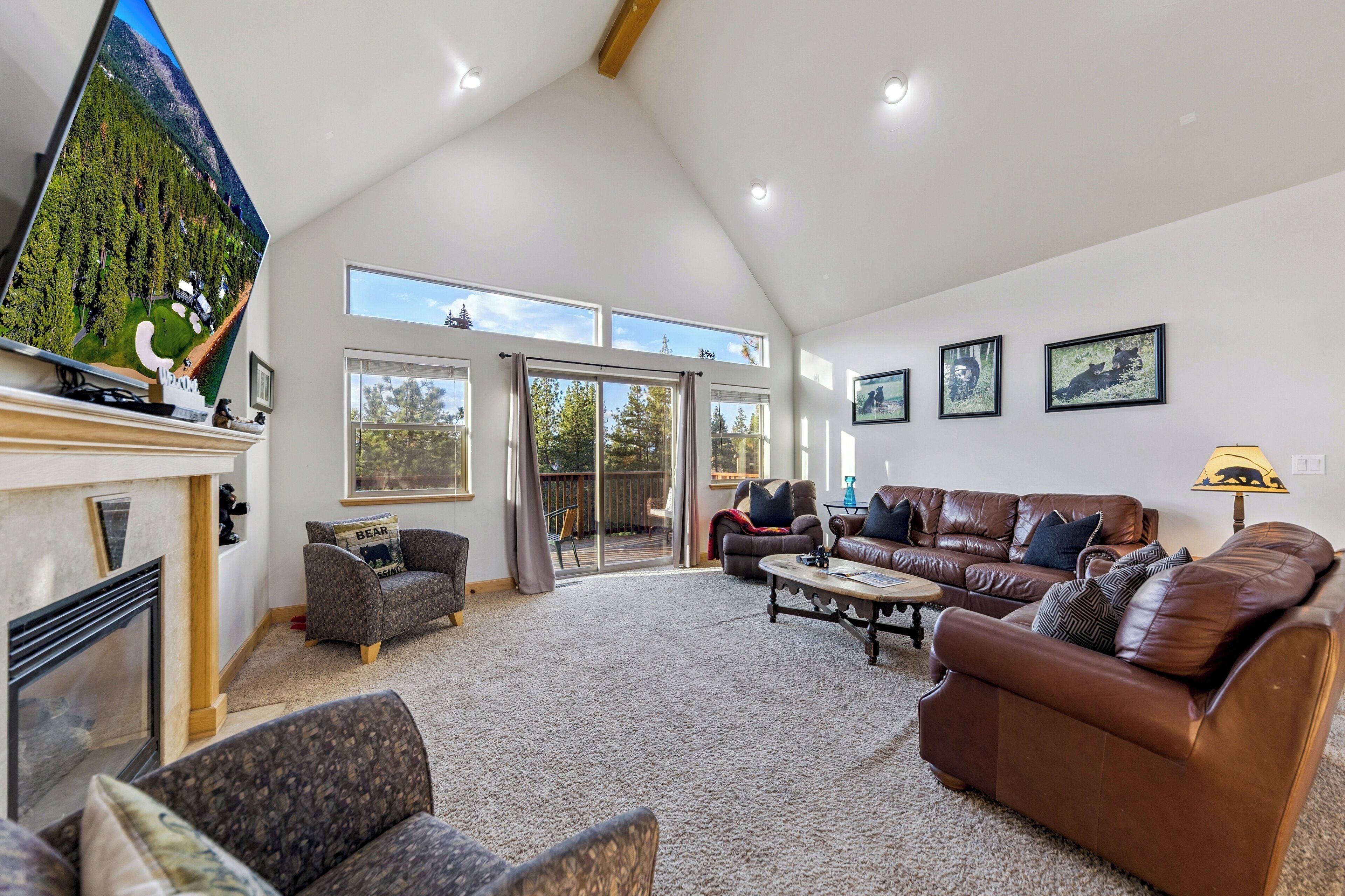 Amplia sala de estar con chimenea, un televisor de pantalla plana grande y una zona de estar cómoda con un sofá de cuero marrón y dos sillones.