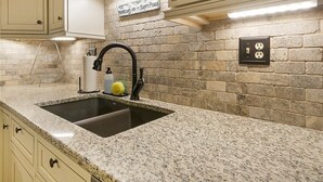 A kitchen with a granite countertop, a black faucet, and a brick backsplash. - Peaks & Peace - Spacious Condo in Silverthorne with jacuzzi and fitness room (Silverthorne)
