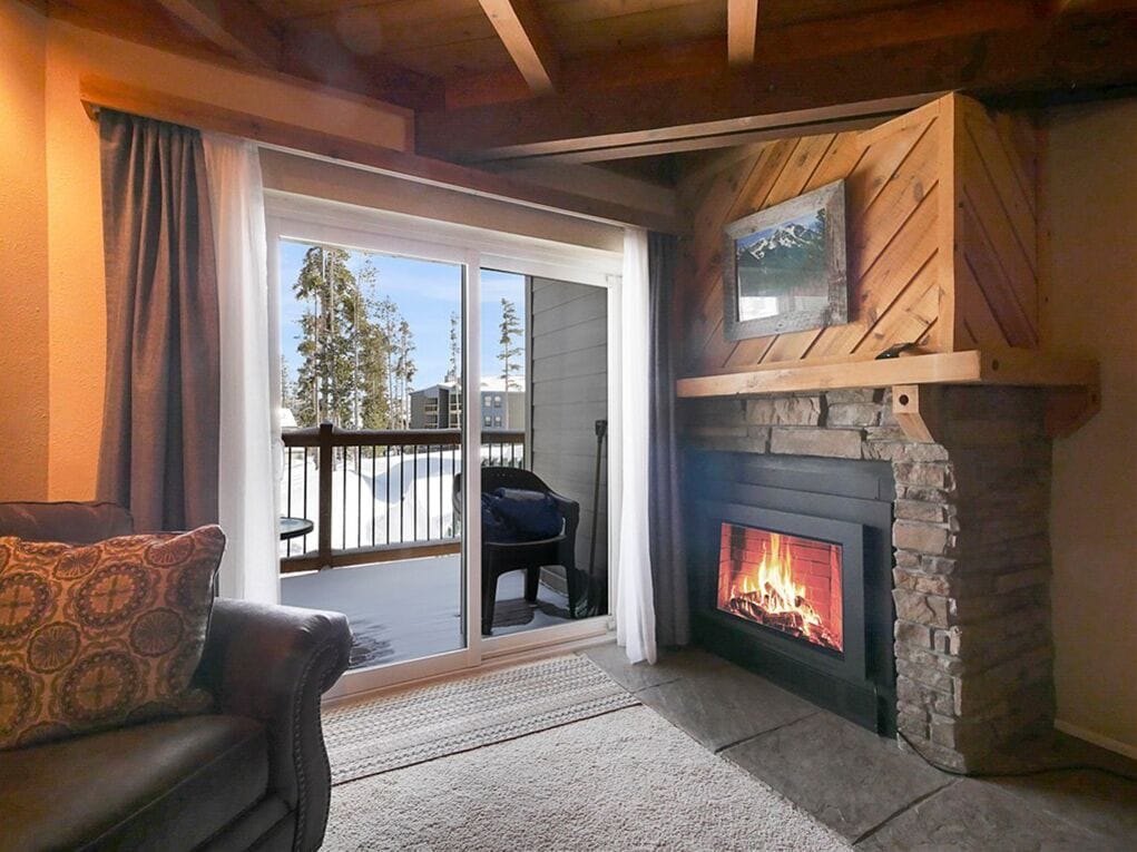 A cozy living room with a fireplace, a sofa, and a sliding glass door leading to an outdoor area.