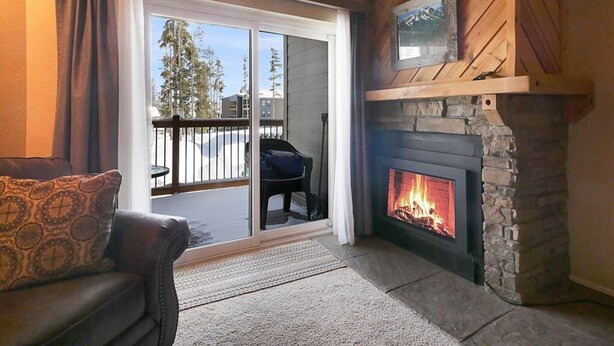 A cozy living room with a fireplace, a sofa, and a sliding glass door leading to an outdoor area. - Peaks & Peace - Spacious Condo in Silverthorne with jacuzzi and fitness room (Silverthorne)