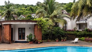Une piscine avec des chaises longues, entourée de plantes en pot et de palmiers.