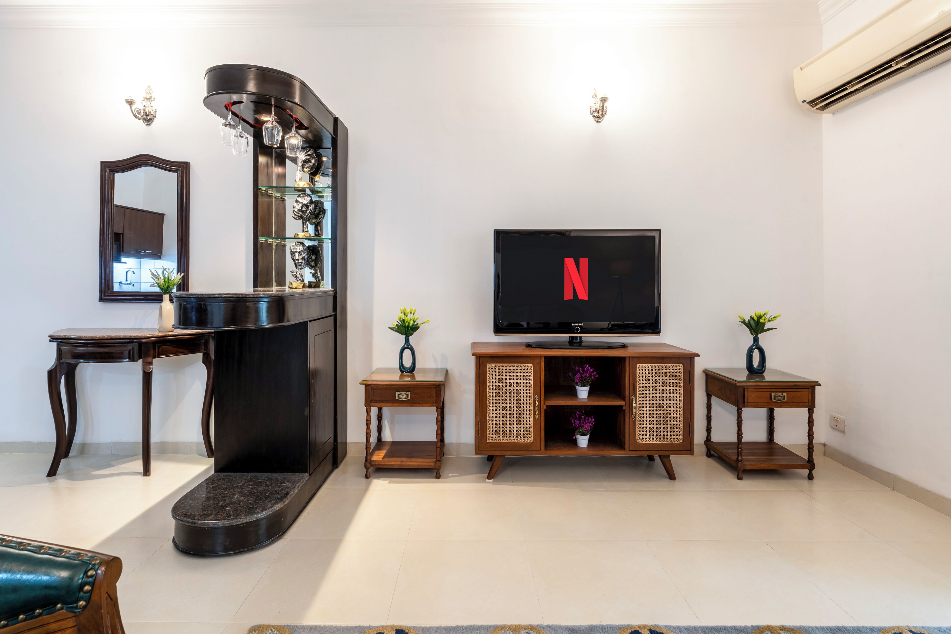 A living room with a TV, a fireplace, a mirror, and two side tables with plants.