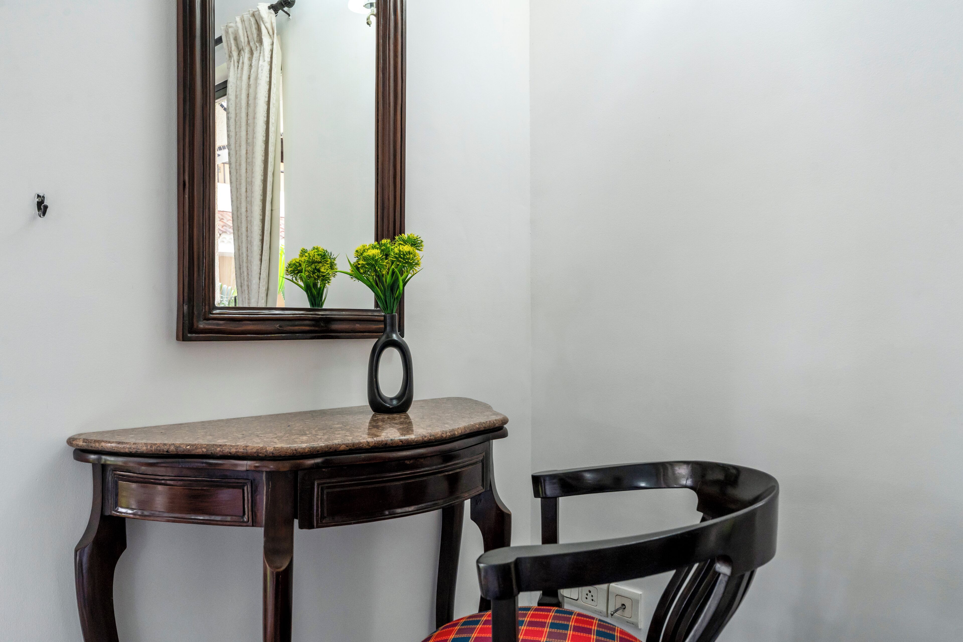 A room with a wooden desk, a chair, a mirror, and a vase with flowers.