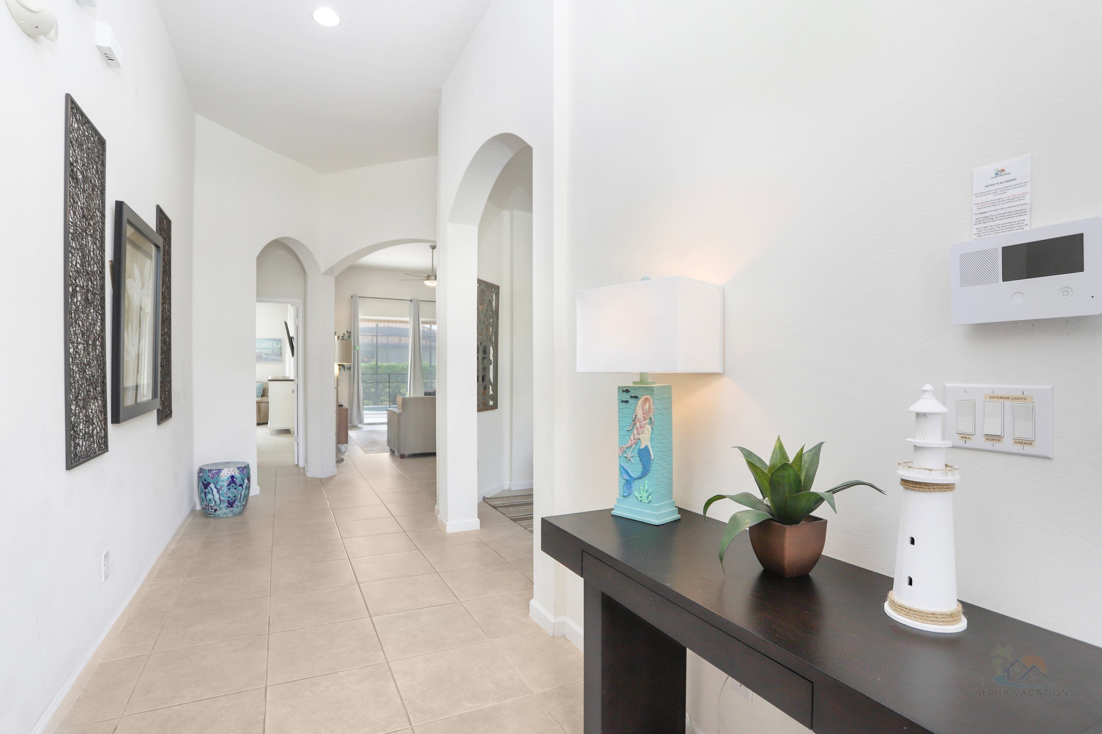 Um corredor com uma mesa consola de madeira escura, uma planta em vaso, uma decoração de farol branco e obras de arte emolduradas nas paredes.