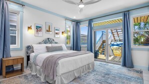 A bedroom with a large bed, a nightstand, a ceiling fan, and a view of a balcony with stairs. - Splash on St. George Island, beachfront, beautiful, close to everything (Eastpoint)