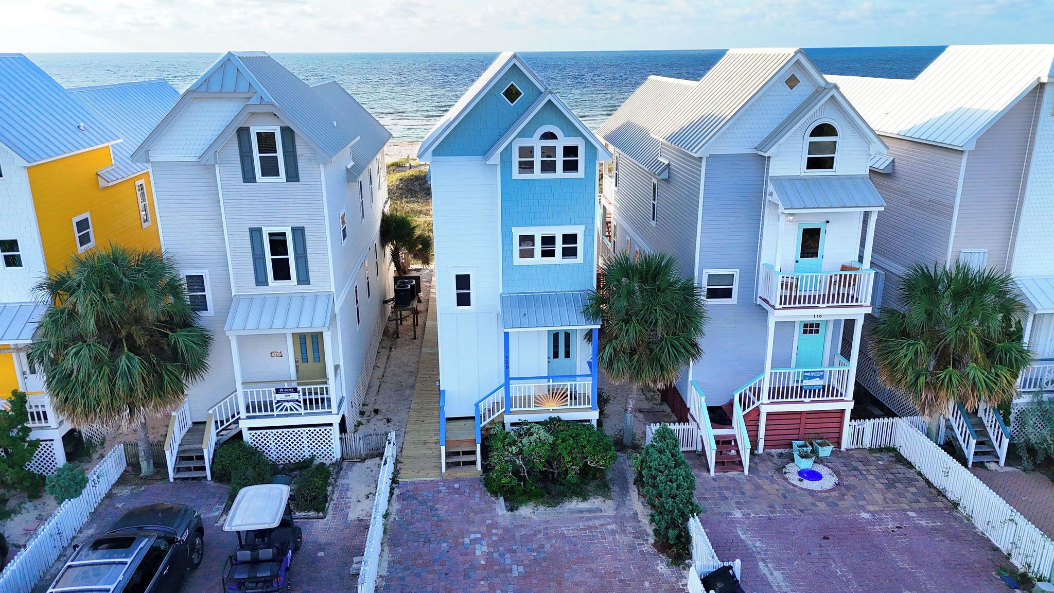 Une rangée de maisons situées en bord de mer, avec une allée étroite menant à chacune d’elles, et chacune possède un petit porche à l’avant et un petit jardin.