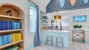 A modern kitchen with a central island, a bookshelf with books, and a neon sign. - Splash on St. George Island, beachfront, beautiful, close to everything (Eastpoint)