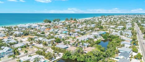 A coastal residential area with houses, a body of water, and a beach in the background.