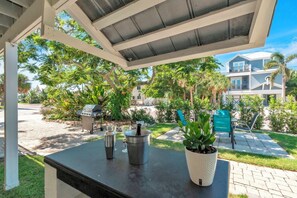A covered patio with a grill, outdoor table, and potted plants.