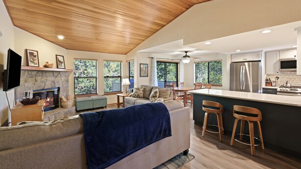 A modern kitchen with a stone fireplace, wooden ceiling, and a large island with bar stools. - Fairway Village 25 - SHARC + Condo Pool, Hot Tub, Near Golf Course, A/C (Sunriver)