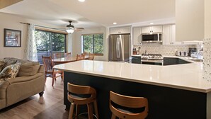 A modern kitchen with a large island, wooden chairs, a dining table, and a ceiling fan. - Fairway Village 25 - SHARC + Condo Pool, Hot Tub, Near Golf Course, A/C (Sunriver)