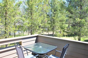A balcony with a glass table and metal chairs, overlooking a forested area.