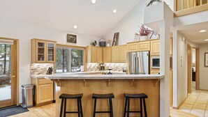 A modern kitchen with wooden cabinets, a large island with stools, and a stainless steel refrigerator. - Cultus 15 - Beautiful, SHARC, Pool Table, A/C, Gas Fireplace (Sunriver)
