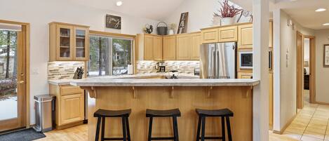 A modern kitchen with wooden cabinets, a large island with stools, and a stainless steel refrigerator.