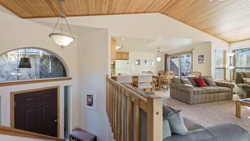 A spacious living area with a wooden ceiling, a sofa, a dining table with chairs, and a kitchen in the background.