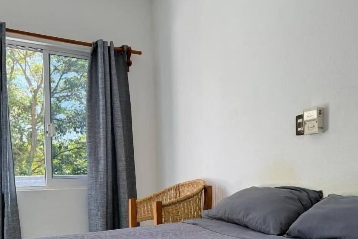 Une chambre à coucher avec un lit, une fenêtre avec des rideaux, une tête de lit et un luminaire fixé au mur.