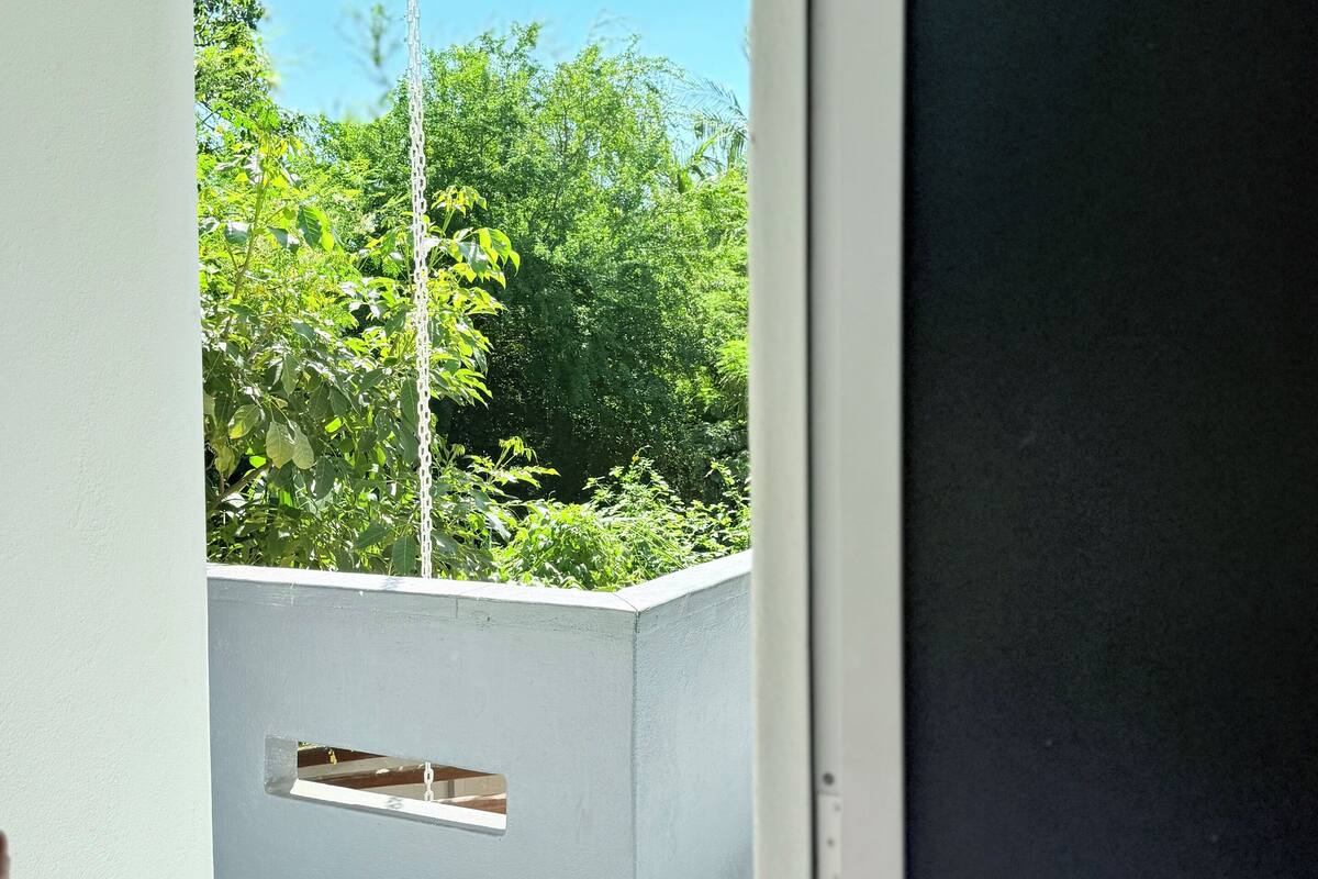 Une vue depuis une pièce dont la porte est blanche, donnant sur un balcon avec une balustrade blanche et une petite fenêtre.