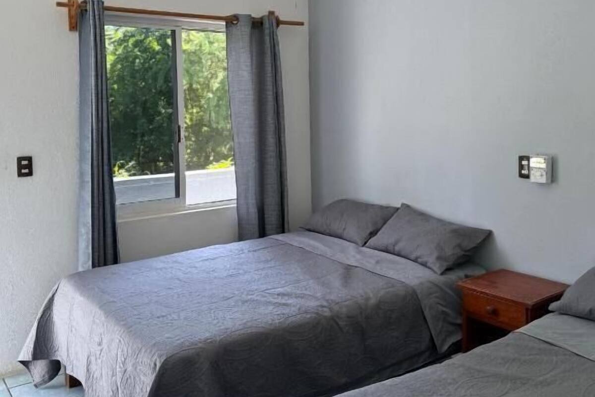 Une chambre avec deux lits, un ventilateur de plafond, une fenêtre avec des rideaux et une table de chevet.