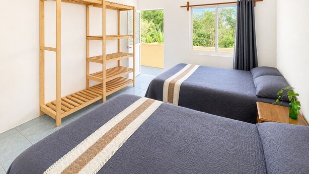 Una stanza con due letti, un mobile contenitore in legno, una finestra con tende e vista sul verde.