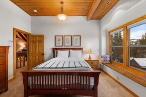 Une chambre à coucher avec un lit en bois, une table de chevet, une fenêtre donnant sur des arbres et un luminaire au plafond.