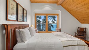 A bedroom with a large bed, wooden headboard, and a window with a view of trees and water. - McKinney Lakeview Lodge in Homewood (Tahoma)